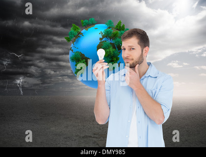 Composite image of handsome model holding a bulb Stock Photo