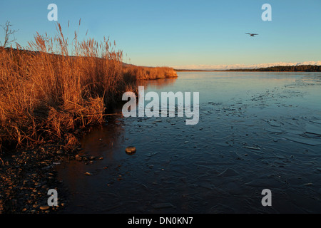 Beluga Lake near Homer Alaska on a fall evening with ice in the water and a small plane coming in. Stock Photo