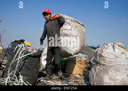 A young child laborer boy is carrying a large sack at the Stung Meanchey Landfill in Phnom Penh, Cambodia. Stock Photo