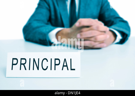 a man wearing a suit sitting in a desk with a signboard in front of him with the word principal written in it Stock Photo