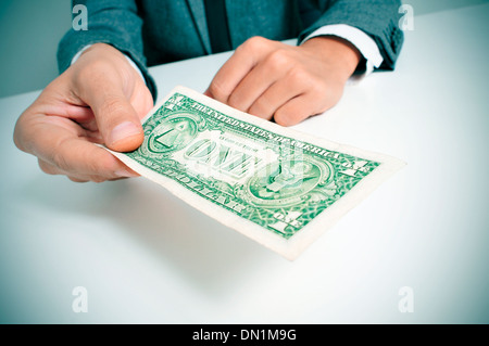 a man wearing a suit sitting in a desk offering a one US dollar bill Stock Photo