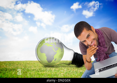 Composite image of thoughtful man sitting on floor using laptop and smiling at camera Stock Photo