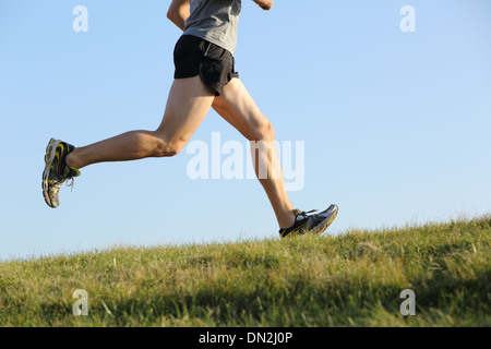 Side view of a jogger legs running on the grass with the horizon in the background Stock Photo