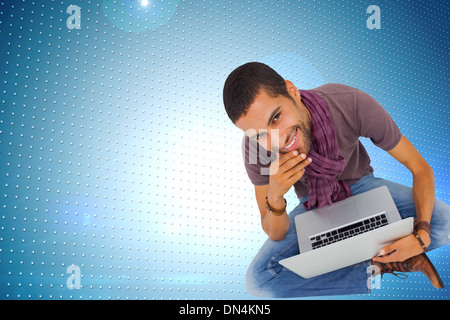 Composite image of thoughtful man sitting on floor using laptop and smiling at camera Stock Photo