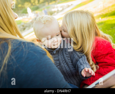 Mother Reading a Book to Her Two Adorable Blonde Children Wearing Winter Coats Outdoors. Stock Photo