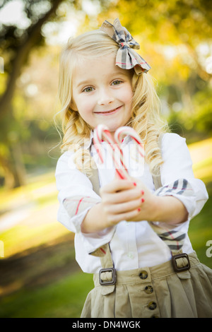 Cute Little Girl with a Bow in Her Hair Holding Her Christmas Candy Canes Outdoors. Stock Photo