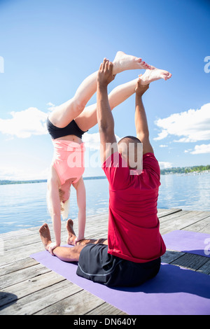 Caucasian couple practicing acroyoga on wooden dock Stock Photo