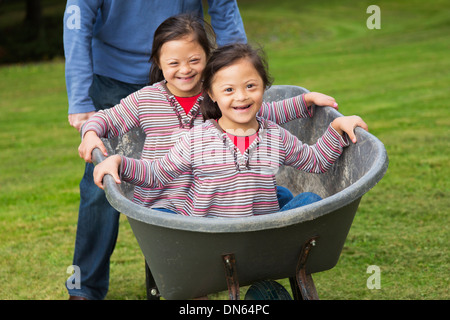 Twins with Down's Syndrome smiling in wheelbarrow Stock Photo