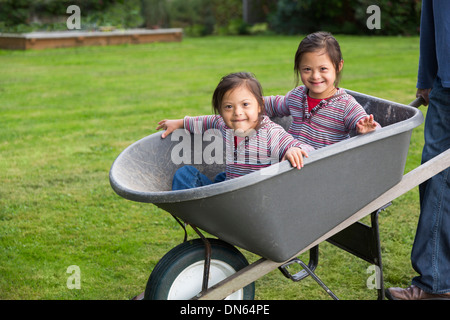 Twins with Down's Syndrome smiling in wheelbarrow Stock Photo