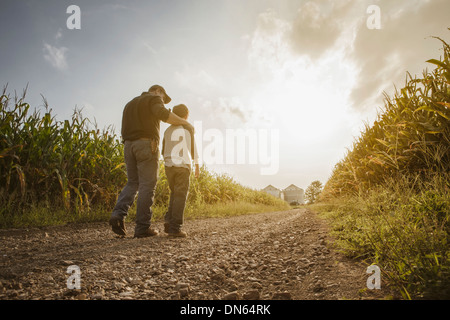 Caucasian father and son walking on dirt road through farm Stock Photo