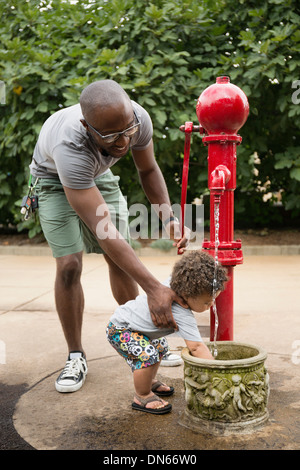 Father and toddler son using water fountain in park Stock Photo