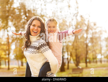 Mother giving daughter piggyback ride in autumn woodland Stock Photo