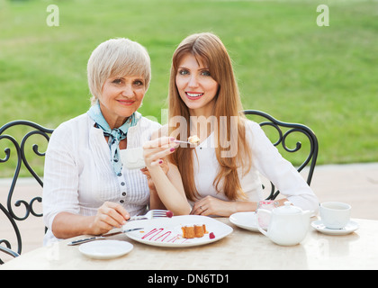 Adult mother and daughter drinking tea or coffee. They communicate sitting outside in a cafe. Stock Photo