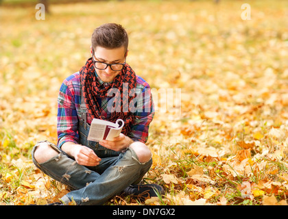 Young hipster relaxed man reading book in nature, back on tree, meadow behind Stock Photo