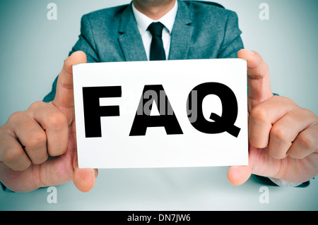 a man wearing a suit sitting in a desk holding a signboard with the word FAQ, Frequently Asked Questions, written in it Stock Photo