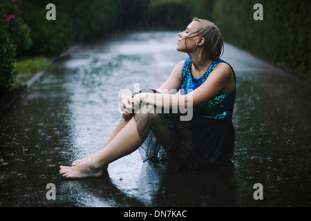 Young woman sitting in rain on the road Stock Photo