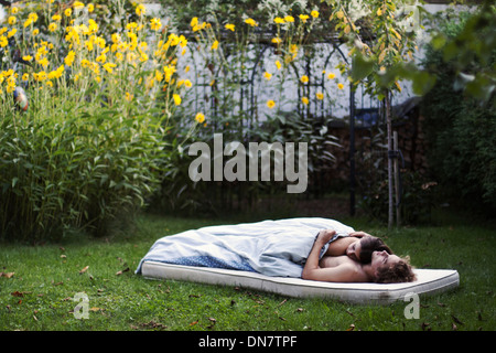 Loving couple lies asleep on a mattress in the garden Stock Photo