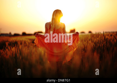 Woman with dress standing in the cornfield at sunset Stock Photo