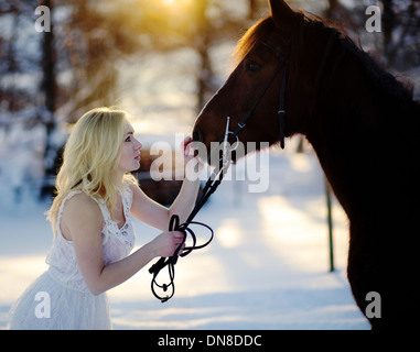 Young woman in white dress with horse in winter Stock Photo