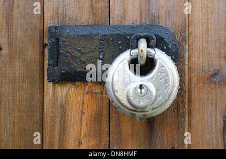 Stainless steel high tensile steel security strength padlock frozen solid from rain overnight  and frost on wooden door Stock Photo
