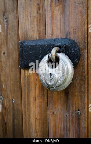 Stainless steel high tensile steel security strength padlock frozen solid from rain overnight  and frost on wooden door Stock Photo