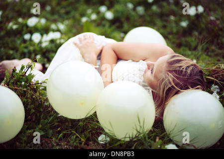 Young woman lying on a meadow between balloons Stock Photo