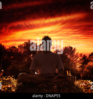 Shaolin Kung Fu instructor meditating in the nature during sunset, sitting with crossed legs under dramatic red sky