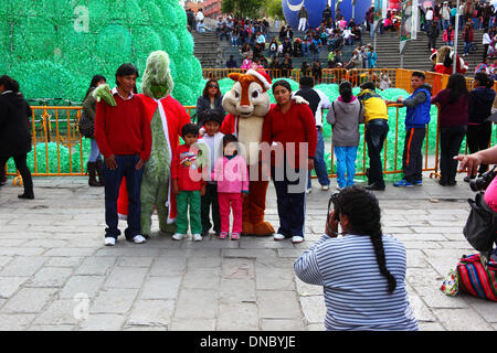 La Paz, Bolivia. 21st December 2013.  A local family poses for instant photos with The Grinch and Alvin the Chipmunk  in Plaza San Francisco. In the background is an ecological Christmas tree made of recycled plastic drinks bottles. The tree is over 15m tall and contains approx. 50,000 bottles. Credit:  James Brunker / Alamy Live News Stock Photo