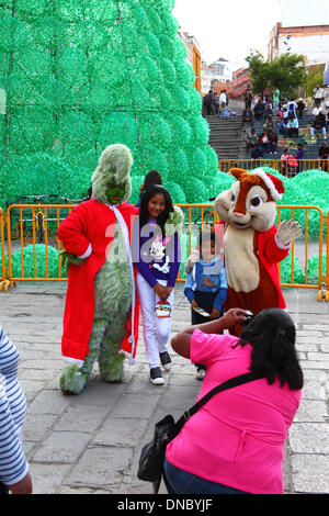La Paz, Bolivia. 21st December 2013.  Locals pose for instant photos with The Grinch and Alvin the Chipmunk in Plaza San Francisco. In the background is an ecological Christmas tree made of recycled plastic drinks bottles. The tree is over 15m tall and contains approx. 50,000 bottles. Credit:  James Brunker / Alamy Live News Stock Photo