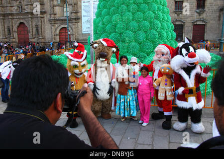 La Paz, Bolivia. 21st December 2013.  An Aymara family pose for instant photos with Santa and popular film / cartoon characters in Plaza San Francisco. In the background is an ecological Christmas tree made of recycled plastic drinks bottles. The tree is over 15m tall and contains approx. 50,000 bottles. Credit:  James Brunker / Alamy Live News Stock Photo