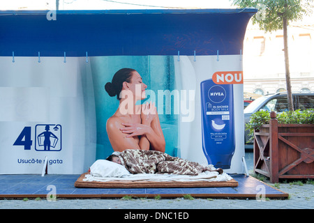 Homeless person sleeping in front of an advert for Nivea in Bucharest, the capital of Romania. Stock Photo