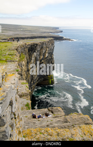 Tourists at steep cliff beside Dun Aengus prehistoric stone fort, Inishmore (Inis Mor), Aran Islands Ireland Stock Photo