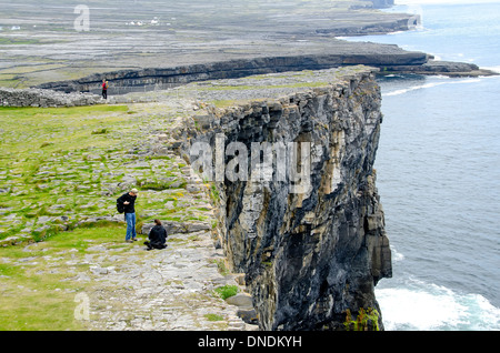 Tourists at steep cliff beside Dun Aengus prehistoric stone fort, Inishmore (Inis Mor), Aran Islands Ireland Stock Photo