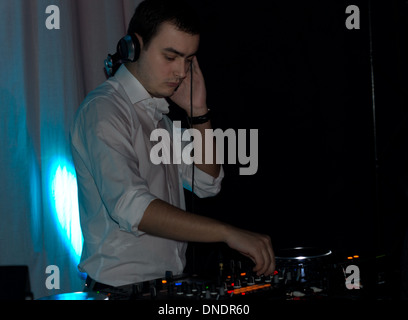 Handsome DJ mixing music on his deck as he provides the dance music at a disco or entertainment venue in a nightclub Stock Photo