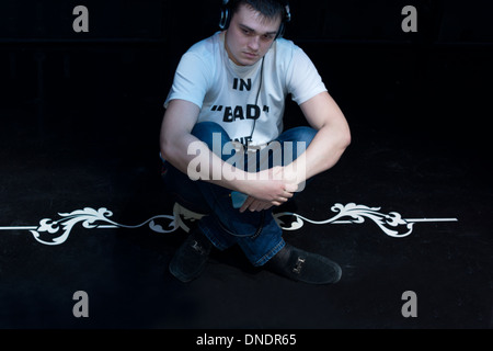 Contented young man sitting cross legged listening to music on his headphones as he relaxes and unwinds in the darkness Stock Photo