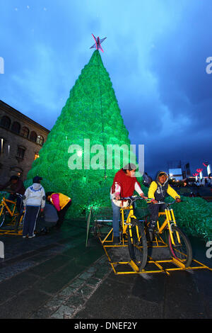 La Paz, Bolivia. 24th Dec, 2013. Locals pedal on bicycles connected to batteries to provide electrical power for the lights on an ecological Christmas tree in Plaza San Francisco. The tree is over 15m tall, contains approx. 50,000 recycled plastic drinks bottles and was a project conceived and planned by the La Paz City Government. Credit:  James Brunker / Alamy Live News Stock Photo