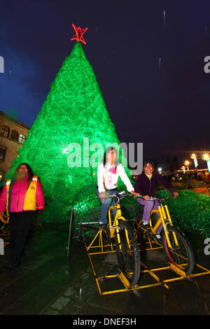 La Paz, Bolivia. 24th Dec, 2013. Locals pedal on bicycles connected to batteries to provide electrical power for the lights on an ecological Christmas tree in Plaza San Francisco. The tree is over 15m tall, contains approx. 50,000 recycled plastic drinks bottles and was a project conceived and planned by the La Paz City Government. Credit:  James Brunker / Alamy Live News Stock Photo