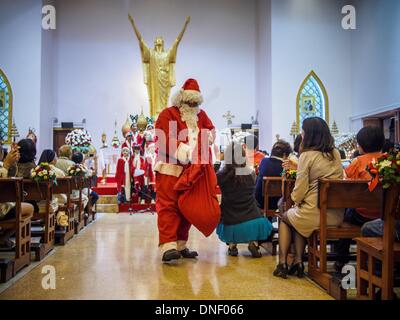 Bangkok, Thailand. 24th Dec, 2013. Santa Claud delivers candy to parishioners during Christmas services at Holy Redeemer Church in Bangkok. Thailand is predominantly Buddhist but Christmas is widely celebrated throughout the country. Buddhists mark the day with secular gift giving but there are about 300,000 Catholics in Thailand who celebrate religious Christmas. Catholics first came to Thailand (then Siam) in 1567 as chaplain for Portuguese mercenaries in the employ of the Siamese monarchy. Credit:  ZUMA Press, Inc./Alamy Live News Stock Photo