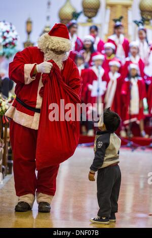 Bangkok, Thailand. 24th Dec, 2013. Santa Claud delivers candy to parishioners during Christmas services at Holy Redeemer Church in Bangkok. Thailand is predominantly Buddhist but Christmas is widely celebrated throughout the country. Buddhists mark the day with secular gift giving but there are about 300,000 Catholics in Thailand who celebrate religious Christmas. Catholics first came to Thailand (then Siam) in 1567 as chaplain for Portuguese mercenaries in the employ of the Siamese monarchy. Credit:  ZUMA Press, Inc./Alamy Live News Stock Photo