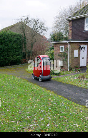 Stationary red mobility vehicle for the disabled parked on a footpath in an estate. Stock Photo
