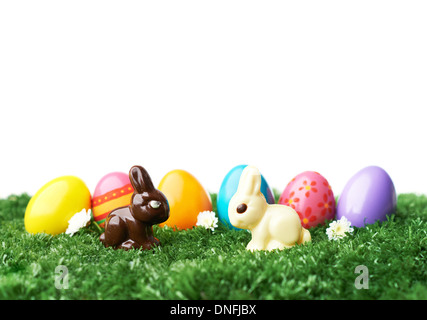 Row of colored and decorated Easter eggs in grass with two chocolate rabbits in front Stock Photo