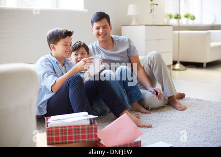 Portrait of cute boy opening envelope with his father and brother near by at home Stock Photo