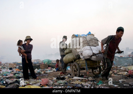 A woman is holding a child while a man pulls a heavy cart at the toxic Stung Meanchey Landfill in Phnom Penh, Cambodia. Stock Photo
