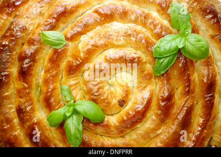 Traditional swirl shaped Balkan pie garnished with fresh basil. Stock Photo