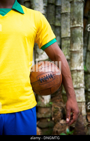Brazilian soccer player standing with old vintage football in front of tropical bamboo jungle background Stock Photo