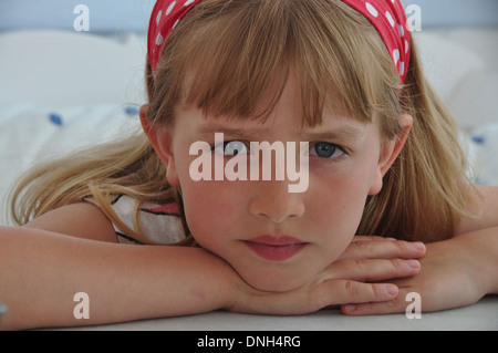 portrait of little blonde girl looking serious and sad looking directly into camera Stock Photo