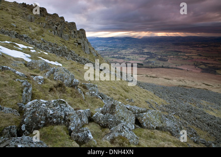 Lichen covered rocks on Clee Hill while the sun shines through the clouds creating Crepuscular rays in the background. Stock Photo