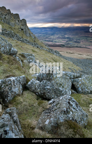 Lichen covered rocks on Clee Hill while the sun shines through the clouds creating Crepuscular rays in the background. Stock Photo