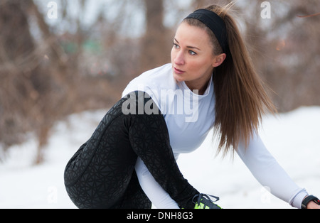 A beautiful young woman stretches before a run on a snow-covered winter day. Stock Photo