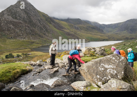Nervous walker being helped across a mountain stream stepping on stones in mountains of Snowdonia. Ogwen Valley North Wales UK Stock Photo